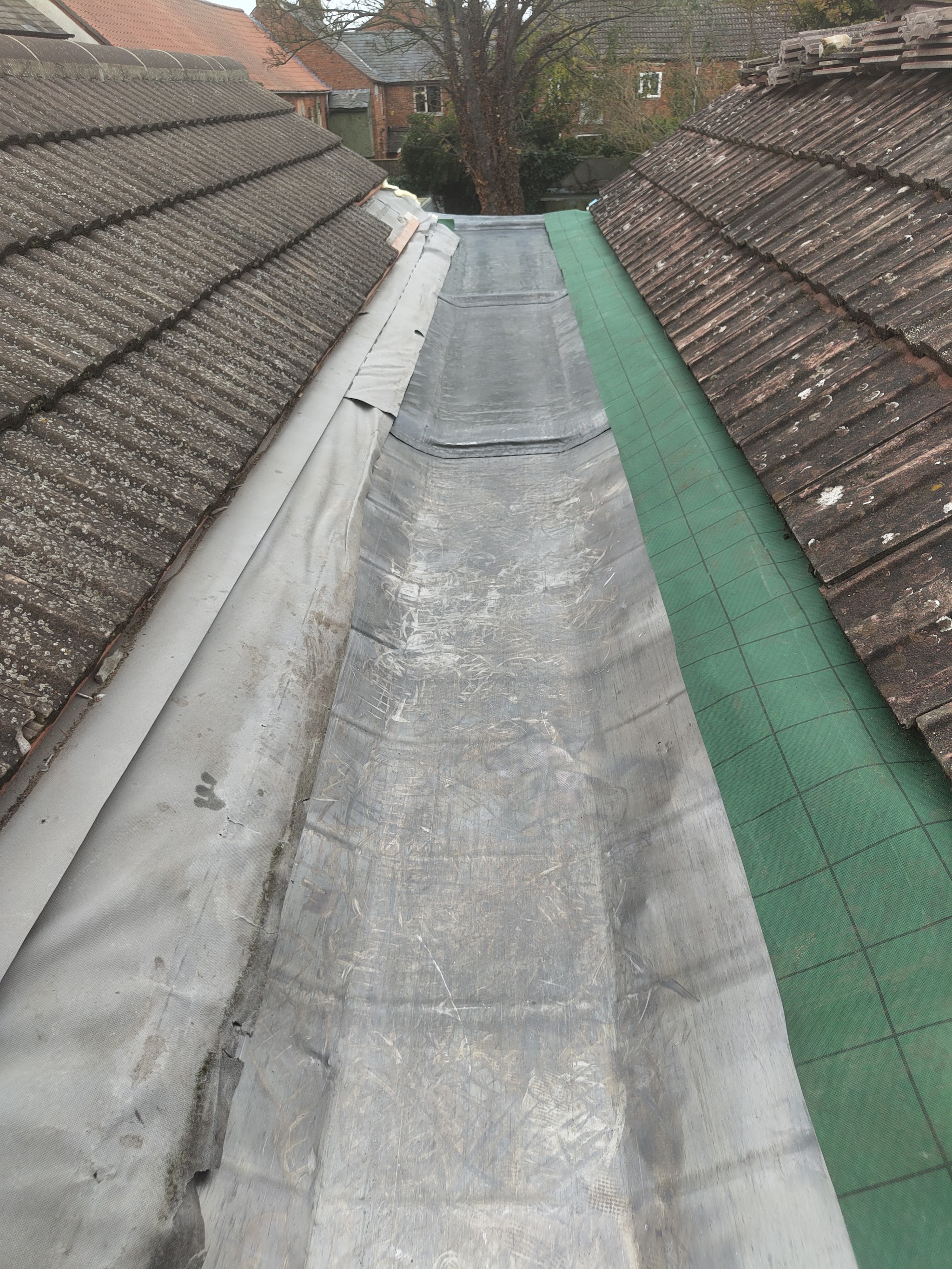 A long roof valley freshly relined between two tiled roof slopes