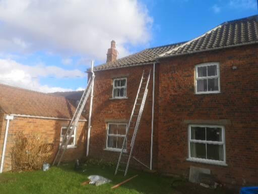 Ladders up against a brick farmhouse during a roofing job